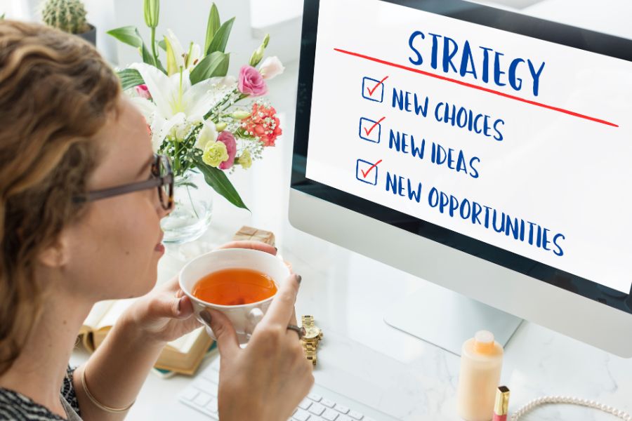 A woman at a desk drinking tea and looking at a computer screen with a "STRATEGY" checklist. A woman at a desk drinking tea and looking at a computer screen with a "STRATEGY" checklist.