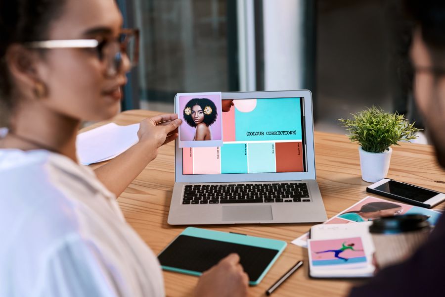 Two designers at a desk comparing a photograph to a color palette on a laptop screen.
