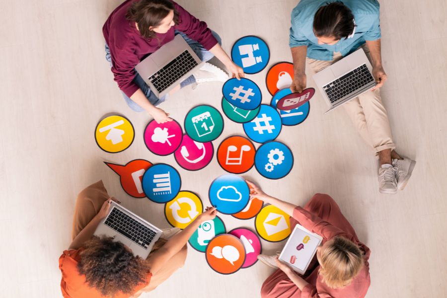An overhead view of four people sitting on the floor, working on laptops around a collection of large social media icons. An overhead view of four people sitting on the floor, working on laptops around a collection of large social media icons.