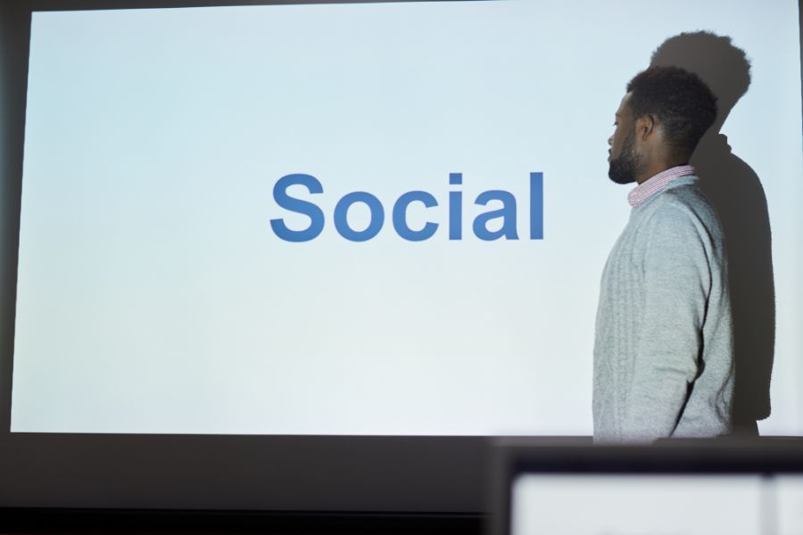 A man standing in front of a projection screen that says "Social." A man standing in front of a projection screen that says "Social."