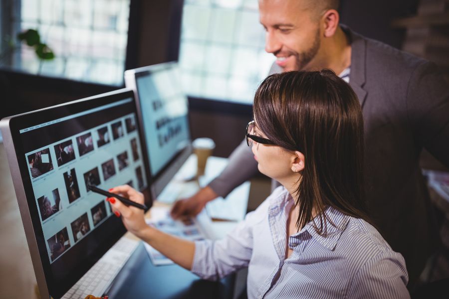 A man and a woman work together, reviewing a gallery of photos on a computer screen in an office. A man and a woman work together, reviewing a gallery of photos on a computer screen in an office.