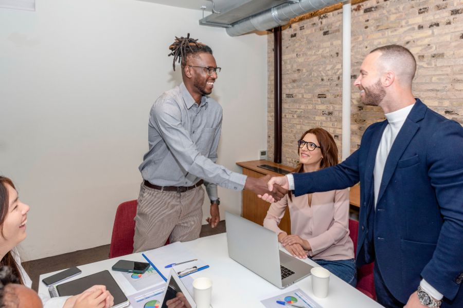 Two men shake hands over a conference table while their colleagues watch and smile. Choosing the Right Dallas Web Design Partner for Your Business