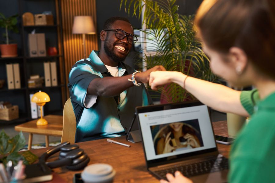 Two colleagues give each other a fist bump over a desk in an office. Two colleagues give each other a fist bump over a desk in an office.