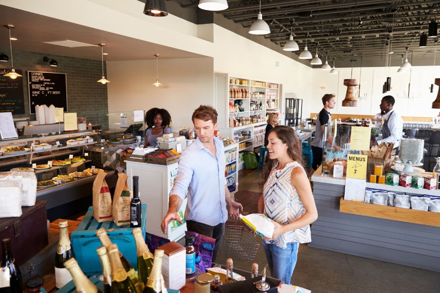 A man and a woman shopping for gourmet food together in a busy delicatessen.