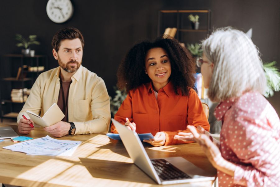 Three diverse colleagues in a meeting, with a senior woman speaking to two younger colleagues.